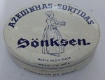 Lata Antiga de Balas "Azedinhas-Sortidas" Sönksen  (C. 1960/70)Rara lata litografada vintage das famosas Azedinhas-Sortidas Sönksen, um dos produtos mais emblemáticos da Chocolate Sönksen S/A. A peça apresenta o design clássico da marca em tons de creme e azul, com a ilustração central da icônica "camponesa" carregando uma bandeja, símbolo que marcou gerações de consumidores em São Paulo