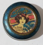 Lata Antiga de Pó de Arroz "Lady"  (C. 1920/30)Raríssima latinha circular de metal do Pó de Arroz Compacto Aderente "Lady". A tampa é uma joia do design gráfico antigo, apresentando a ilustração central de uma jovem com penteado clássico da época, cercada por flores e molduras decorativas. As cores vibrantes em azul, dourado e tons rosados refletem o luxo e o refinamento dos produtos cosméticos daquela era.