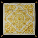 ATELIER VERSACE  Manta representando a clássica estampa  Baroccoo em tons de amarelo e dourado sobre fundo claro. Confeccionado em seda pura ou misturas luxuosas de seda e modal. Dependendo do tamanho e acabamento (como a presença de franjas ou bordas enroladas), pode ser utilizado como lenço de pescoço, xale ou até mesmo como um item decoração para casa. 136 x 136 cm.