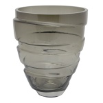 Vaso singular de formato cônico, em cristal levemente fumê, construído com faixa encaracolada em relevo. Borda lisa e base retraída e circular. 25 x 21 cm.