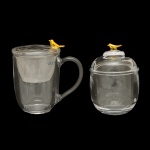 WOLFF  Conjunto de 2 peças para chá em vidro translucido  da manufatura nacional. Tampa com detalhe de pássaro dourado, sendo: 1 caneca com filtro infusor de aço inox (13 x 12 cm) e 1 açucareiro (12 x 8 cm).