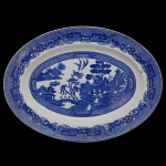 HUGHES LONGPORT. Inglaterra - Travessa oval em louça inglesa decorada com a famosa estampa blue willow (Salgueiro Azul), Dois pássaros voando juntos no topo, representando as almas dos amantes transformados e centro com castelos e jardins. 37 x 27 cm.