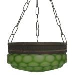 Luminária de teto suspensa, caracterizada por uma cúpula circular de vidro verde texturizado em relevo que lembra colmeia e estrutura de metal texturizado sustentada por correntes. Estrutura presa por três correntes metálicas interligadas que convergem no topo. 102 x 27 cm.
