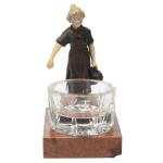 Escultura em bronze patinado retratando uma figura feminina, representando uma camponesa, montado em base de mármore, acompanhando de um recipiente de cristal. 15 x 8 x 10 cm (MT). 4 x 7 cm (cristal)