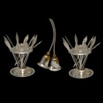 Lote constando de 3 peças em metal prateado, sendo: suportes com espetos para aperitivos (12 x 8 cm) e 1 campainha de mesa dupla na forma de flor (16 x 8 cm).