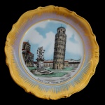 Prato em porcelana italiana retratando a paisagem da Torre de Pisa na Itália, com acabamento dourado na borda. 26 cm.