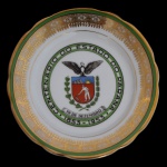Prato em porcelana nacional da manufatura Real, comemorativo do Centenário do Estado do Paraná. Apresenta o brasão de Armas do Paraná ao centro circundado pela inscrição Centenário do Paraná (1853-1953), decorado com bordas trabalhadas e detalhes em verde e filetes de ouro. 18 cm. Apresenta um lascado no verso do prato.