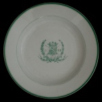 Prato em porcelana holandesa decorado em verde, com borda lisa, centralizando brasão de armas sob coroa, ladeado por louros. Apresenta personagem sobre a legenda De Gentsche Shutter (O Atirador de Ghent). Etiqueta de colecionador sob a base. 23 cm.