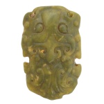 Antigo passador de cinto chinês em jade verde, representando máscara de divindade protetora. 7 x 4 cm.