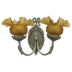 Luminária arandela de parede com estilo clássico e cúpulas em formato de tulipa cor âmbar. Apresenta uma base metálica com detalhes ornamentados e hastes curvas que suportam duas luzes.