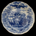 Prato em louça inglesa apresentando uma ilustração detalhada em tons de azul cobalto sobre fundo branco, retratando paisagens rurais com carruagens e cavalos. Marcas da manufatura Oxford, Brasil no verso. 23 cm.