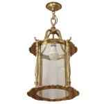 Luminária de teto para uma lâmpada, na forma de lanterna em latão polido dourado, estilo francês, e painéis de vidro curvo transparente. Modelo cilíndrico  com armação metálica dourada, acabamento ornamentado nas bordas superior e inferior, unida por colunas verticais trabalhadas de forma delicada. Muito utilizado na iluminação de halls de entrada, varandas e corredores de casas de época. 67 x 33 cm.