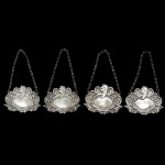 Conjunto de 4 marcadores de garrafas antigos, também conhecidos como dísticos ou etiquetas para decantadores, em metal prateado. Apresentam ornamentos detalhados em alto relevo, com volutas e motivos florais, Destinados a identificar o conteúdo de garrafas de bebidas finas como Whisky, Porto, Campari e Cognac. 6 x 7 cm. 14 cm (com a corrente).