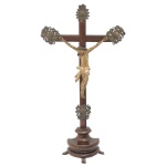 Singelo crucifixo de mesa antigo, frequentemente denominado "crucifixo de pousar". Cruz em madeira, com a figura de Cristo também em madeira policromada. Apresenta resplendor e ponteiras ornamentais em metal. 57 x 30 cm (MT). 23 x 18 cm (Cristo). 16 x 7 cm (base).