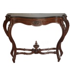 Mesa de encostar estilo neorrococó, em madeira nobre, ornado por molduras lisas. Tampo recortado e bordado por canelados. Saia seguindo o movimento, centralizando composição naturalística em medalhão oval. Pernas curvilíneas, com joelhos proeminentes recamados por adornos vegetais, e rematadas por sapatas. Base com amarração em X e traves recurvas realçadas por adorno no formato de pião com ponteira. Séc. XIX. 93 x 118 x 42 cm.