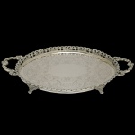 Bandeja em prata de lei brasileira, repuxada e cinzelada, de formato oval com galeria vazada e ornada por volutas. Centro gravado e ornamentado com larga guirlanda plumada. Alças laterais em meia argolas estilizadas e pés de garra encimados por folhagens. Contraste do teor de 833 mls. 45 x 27 cm. Peso aprox..110 gramas.