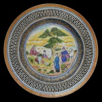 Prato de porcelana chinesa Cia das Índias apresentando figuras ao centro com árvores e jardim. Decoração rouge de fer com frisos azul cobalto. Larga faixa vazada na borda. 25 cm.