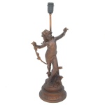 Luminária de mesa montada com escultura em petit bronze patinado representando anjinho de braços abertos, segurando ramo florido, de pé sobre base cônica decorada por adornos estilizados. Haste central reta rematada por bocal. 40 x 56 cm (escultura). 54 cm total (MT).
