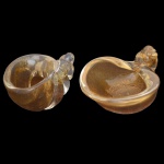Conjunto de duas conchas em vidro artístico de Murano, produzida na Itália, possivelmente por Seguso Vetri d'Arte. Apresenta detalhes em flocos de ouro em tom champanhe, com detalhes que podem incluir folha de ouro. 5 x 10 x 6 cm / 4 x 10 x 9 cm.