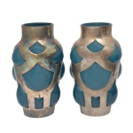 Par de vasos de vidro decorativos com metal de formato cilíndrico realçados saliências semiesféricas, revestidos por montagens vazadas em metal prateado liso. Detalhes em tom azul-escuro contrastando com uma estrutura fosca ou metalizada. 18 x 10 cm.