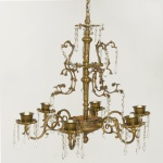Elegante lustre para 6 luzes em bronze ormolu. Coluna central reta apoiada em meia cúpula ornada por perolados, sustentando hastes em S, rematadas por bobeches bordadas por placas em cristal lapidado e encimados por pequenos copos. Apresenta a meia altura anelados ladeados por grande adornos com arabescos acoplados e pingentes facetados. Parte superior com pequeno plateau acompanhando a decoração. 128 x 56 cm.