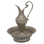 Pequeno gomil e bacia em metal prateado, comumente utilizado para toalete ou fins litúrgicos. Apresentam decoração canelada com gomos torcidos. 30 cm (MT). 30 x 15 cm (jarra).  9 x 25 cm (bacia).