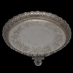 Pequena salva circular em prata de lei, repuxada e cinzelada. Centro com decoração de guirlanda de flores e folhas. Borda decorada com estilizações.  No verso marca do teor 833. 12 cm. Peso 158 gramas.