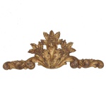 Talha de parede em madeira esculpida e dourada, de formato alongado. Apresenta ornamentação esculpida por volutas e folhagens, encimada por composição central realçada por flores e pétalas. Essas peças são comumente utilizadas em projetos de design de interiores e arquitetura para ornamentar paredes, tetos (boiseries), molduras de portas, móveis ou até altares. 27 x 71 cm.