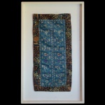 Painel de parede montado com bordado chinês de seda policromada e bordada. Apresenta margem com motivos geométricos e flores, centralizando painel ornado por 2 faixas com adornos florais sobre fundo azul. Moldura em madeira branca. 67 x 40 cm (ME).