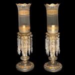Belíssimo par de castiçais em cristal, profusamente decorados a ouro e realçados por discretos adornos florais policromados. Colunas centrais retas e ornadas por anelados e carreteis. Bobeches circulares, bordadas por pingentes facetados. Mangas cilíndricas com bordas reviradas e dentadas. Hastes curtas apoiadas em bases circulares moldadas com degraus. 57 x 33 cm (MT). 20 cm (cúpula). 18 cm (base).