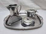 Lote de jarra, açucareiro, manteigueira, porta guardanapos e bandeja em aço inox. Medindo a bandeja 39cm x 24cm.