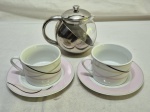 Lote de bule em metal prateado com recipiente em vidro e 2 xícaras de chá em porcelana. Medindo o bule 11cm de altura. O pires com fio de cabelo.