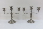 Par de candelabros para trs velas em metal espessurado à prata, base circular , haste central em formato balaústre e dois braços curvos. Med. 25 x 27 cm.