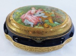 LIMOGES, França - Grande caixa porta joias oval em fina porcelana francesa esmaltada na tonalidade azul cobalto, ornada com cena galante com realces em fio de ouro brunido 24k , borda decorada com guirlanda e guarnições em bronze. Marcada no fundo. Medidas: 10 cm altura x 21 cm comp x 15 cm diâmetro.