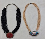 Duas (02) gargantilhas com múltiplos fios, uma com pérola sintética e pingente esmaltado em tons azul e contas e um na cor preta com ´pingente em metal com placa na cor CORAL. Medida aberto 50 cm comprimento.