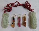 Cinco (05) peças ,sendo três figas em pedra ágata com detalhes e acabamento em dourado. ( 3 cm comprimento) e, dois pingentes de jadeita esculpido representando a Figura de Guanyin ( A Deusa da misericórdia , significa compaixão, amar e proteção ( 4,5 cm comprimento).