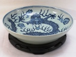Grande fruteira/Medalhão em pesada porcelana oriental azul. Decoração típica da Ming do Reinado com dragão central e pérolas de fogo. Acompanha grande peanha em madeira torneada e entalhada. Med. 8 x 36 cm- peanha 4,5 x 31 cm.