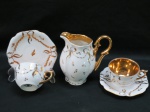 Duas (02) xícaras para café e uma cremeira de coleção, interior pintadas a mão em ouro 24 K, em porcelana branca,decorada com laços de fita e detalhes em dourado. Med. cremeira 11.5 cm.