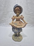 Linda escultura de menina com vestido e chapéu em resina com policromia, assinado. Medindo 27,5cm de altura.