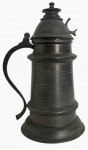 Caneca antiga em estanho, com tampa articulada, corpo cilíndrico com frisos, alça vazada e acabamento em pátina escura. Peça de estilo europeu, ideal para coleção ou decoração. Mede 28cm.