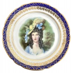Prato decorativo em porcelana europeia, com retrato feminino em estilo clássico ao centro, cercado por rica borda em azul cobalto com douração e detalhes ornamentais. Verso com marca São Paulo, indicando peça de circulação nacional. Apresenta leves sinais de uso e desgaste compatíveis com o tempo. Mede 23cm.
