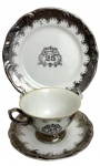 Trio para chá contendo uma xícara, pires e prato em porcelana Porcelana Real, com decoração em prata e inscrição comemorativa Bodas de Prata  25 anos. Peças com acabamento clássico e relevo na borda, apresentando sinais de uso e desgaste na metalização.