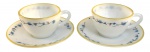 Par de xícaras de café com pires em vidro opalinado, apresentando delicada decoração floral estilizada em tons de azul e preto, com filetes dourados na borda. Peças de estética elegante, possivelmente meados do século XX, com leve translucidez e bom estado geral.