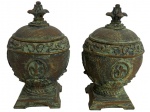 Par de potiches em resina com pátina verde e dourada, com tampa, decorados em relevo com motivos clássicos e flor-de-lis. Bases quadradas e puxadores em forma de flor. Peças de caráter ornamental, com pátina intencional e leves marcas do tempo. Mede 18cm.
