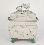 Antiga terrina / caixa em porcelana esmaltada, de formato retangular, com decoração delicada representando aves (garças) em relevo sobre paisagem, distribuídas por toda a superfície. Tampa encimada por elemento escultórico figurativo. Base elevada sobre quatro pés, com detalhes em tonalidade verde. Medidas: 32 cm (altura) x 23 cm (comprimento) x 18 cm (largura). Craquelê natural da antiguidade. Apresenta restauros na tampa e base. Um pé necessita restauro.