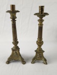 Arte Sacra. Dois castiçais de altar em bronze, com base tripé ricamente decorada em relevo e coluna canelada de inspiração neoclássica. Peças de uso litúrgico/devocional, com pátina natural e marcas do tempo. Alturas: 28 e 29 cm.