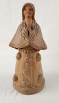 Escultura em cerâmica representando figura feminina, de caráter simbólico, com base decorada por rostos estilizados. Peça de arte popular brasileira, modelada manualmente, com acabamento rústico e assinatura `Lídia` na base. Altura: 27 cm.