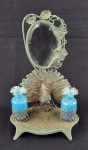 Conjunto de toilette Art Nouveau em metal fundido com pátina, composto por espelho bisotado central e dois recipientes em vidro azul, decorado com figura de pavão em relevo. Medidas: 30 x 20 x 11 cm. Apresenta marcas do tempo. 