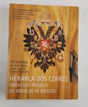 Livro de arte intitulado Herança dos Czares – Obras dos Museus do Kremlin de Moscou, publicado pela Fundação Armando Alvares Penteado em parceria com o Museu de Arte Brasileira, reunindo importante acervo histórico-cultural do Kremlin de Moscou. A obra apresenta rica iconografia com peças ligadas à realeza russa, como joias, insígnias, objetos litúrgicos e arte decorativa, ilustrando o legado dos czares. Exemplar em capa dura com sobrecapa ilustrada em fundo dourado e brasão imperial, em bom estado geral, podendo apresentar leves sinais de manuseio compatíveis com o uso. Ideal para colecionadores, estudiosos e apreciadores de arte e história. 