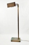 Luminária de piso em metal dourado e bronze, medindo aproximadamente 104 cm de altura, composta por haste longa sobre base retangular com pedra interna para estabilidade. Fiação com interruptor no cabo. Necessita revisão. Apresenta sinais de uso e pátina do tempo, com marcas no metal e desgaste compatível com a idade, além de oxidação em pontos da estrutura e base.